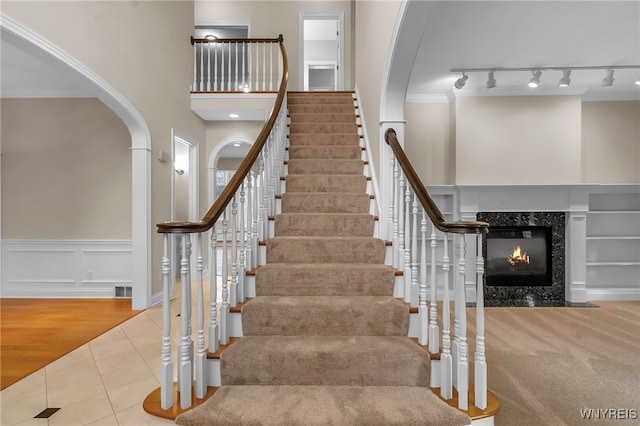 stairway featuring tile patterned floors, crown molding, and a high end fireplace