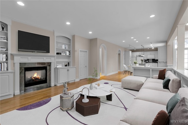 living room with a high end fireplace, built in shelves, and light wood-type flooring