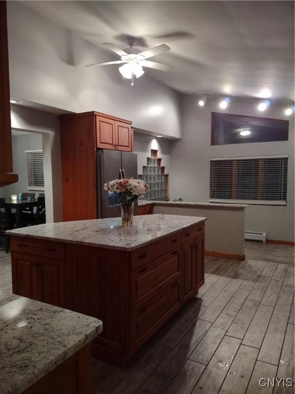 kitchen with a kitchen island, a baseboard heating unit, stainless steel fridge, ceiling fan, and light stone counters