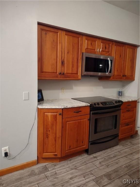 kitchen with stainless steel appliances, light hardwood / wood-style flooring, and light stone countertops