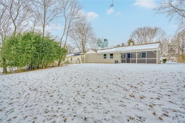 snow covered back of property featuring a sunroom