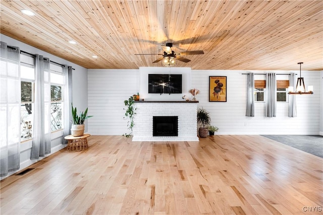 interior space with wood walls, wood ceiling, light wood-type flooring, ceiling fan with notable chandelier, and a fireplace