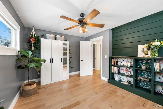 interior space featuring light wood-type flooring, ceiling fan, and wooden walls