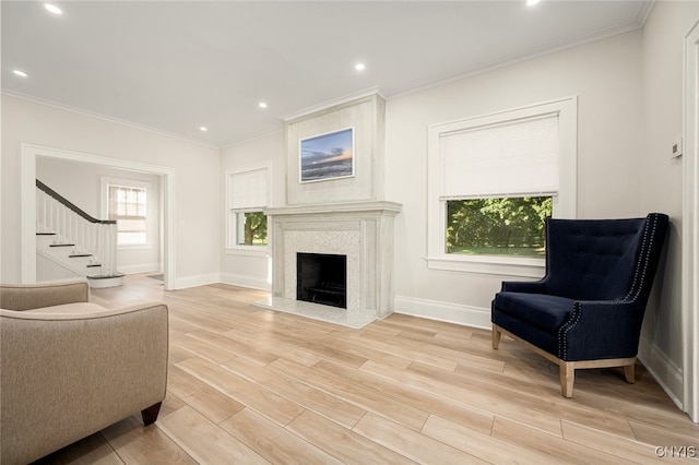 living area with a high end fireplace, light hardwood / wood-style flooring, a wealth of natural light, and crown molding