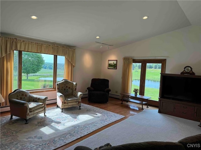 living room with light wood-type flooring, a water view, vaulted ceiling, and a baseboard heating unit