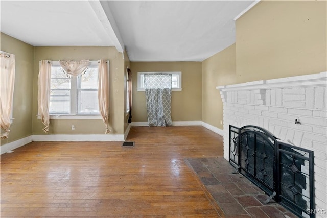 living room featuring beamed ceiling, wood-type flooring, and a brick fireplace