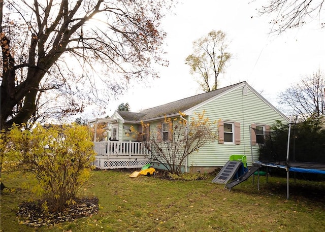 rear view of property featuring a yard, a deck, and a trampoline