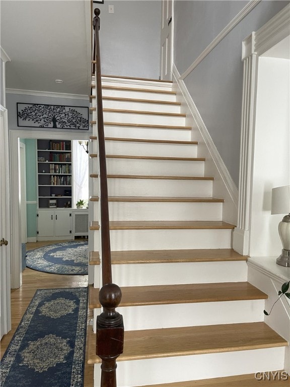 staircase featuring ornamental molding, wood-type flooring, and built in shelves