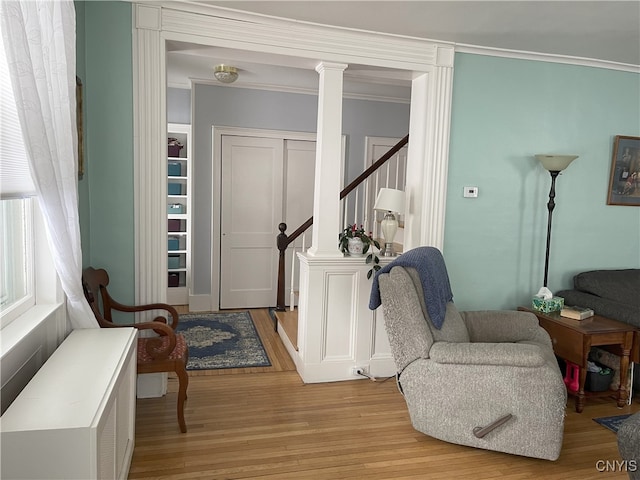 living area with ornate columns, ornamental molding, and light hardwood / wood-style floors