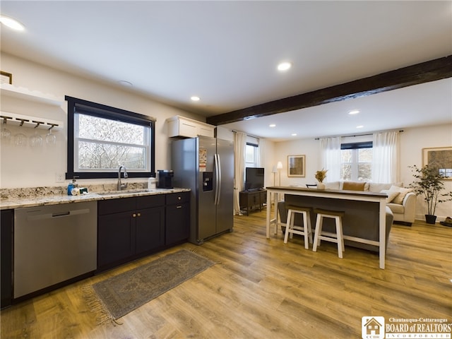 kitchen featuring beam ceiling, light stone countertops, sink, stainless steel appliances, and light hardwood / wood-style floors