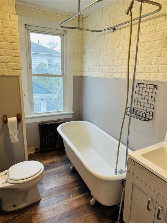 bathroom with vanity, hardwood / wood-style flooring, toilet, radiator heating unit, and a tub