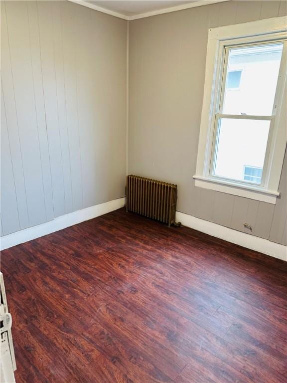 spare room featuring dark hardwood / wood-style flooring, radiator heating unit, and ornamental molding