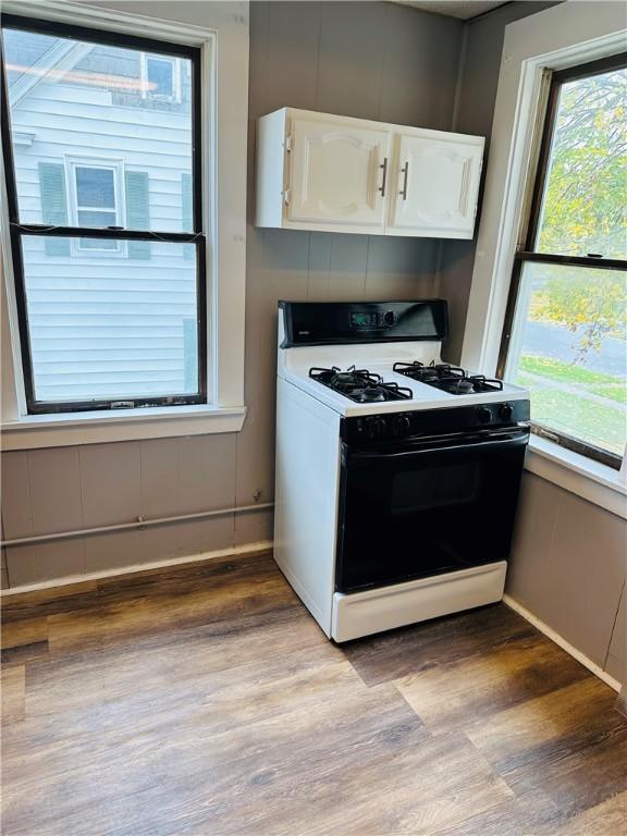 kitchen with white range with gas stovetop, white cabinets, light hardwood / wood-style flooring, and a wealth of natural light