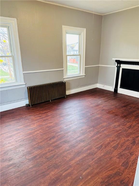 unfurnished living room featuring radiator heating unit, ornamental molding, and dark wood-type flooring