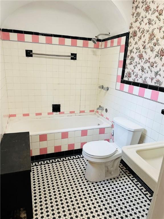 bathroom with tile patterned floors, tiled shower / bath combo, toilet, and tile walls