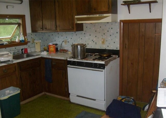 kitchen with dark brown cabinetry, tasteful backsplash, white gas stove, and sink