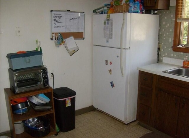 kitchen with tasteful backsplash, dark brown cabinets, white fridge, and sink