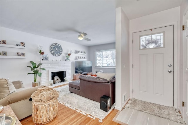 foyer entrance with light hardwood / wood-style flooring, a brick fireplace, and ceiling fan