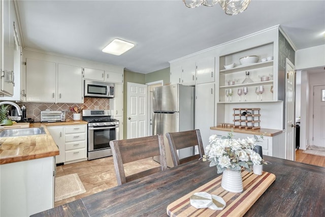 kitchen with appliances with stainless steel finishes, tasteful backsplash, sink, white cabinets, and butcher block counters