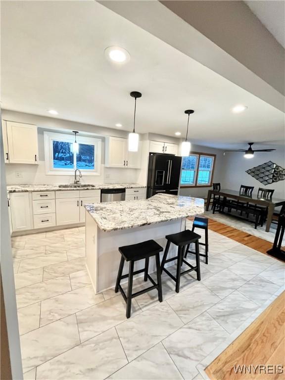 kitchen featuring sink, a kitchen island, black refrigerator with ice dispenser, pendant lighting, and white cabinets