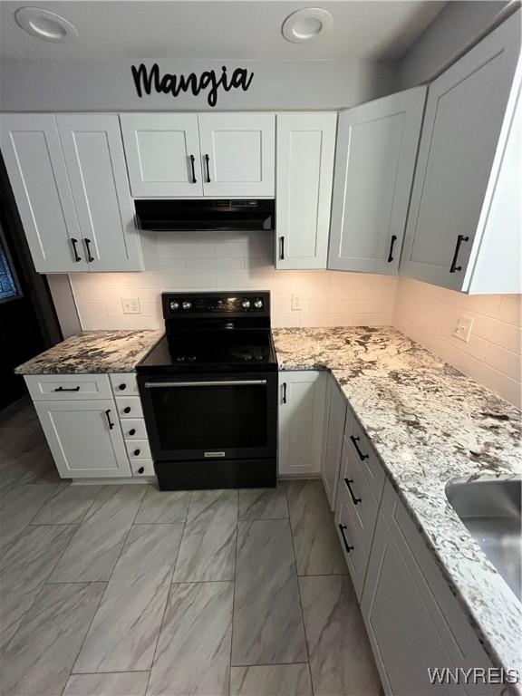 kitchen featuring light stone countertops, backsplash, white cabinetry, and black electric range oven