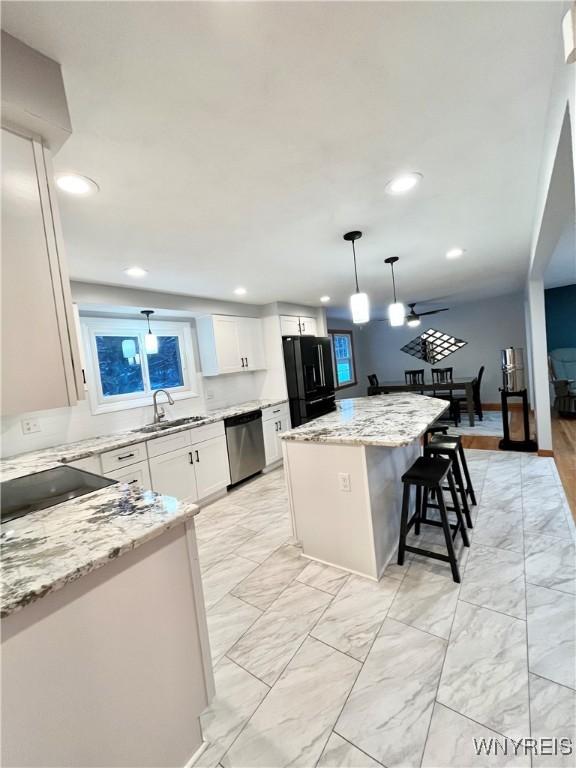 kitchen featuring white cabinetry, sink, black fridge, decorative light fixtures, and a kitchen island