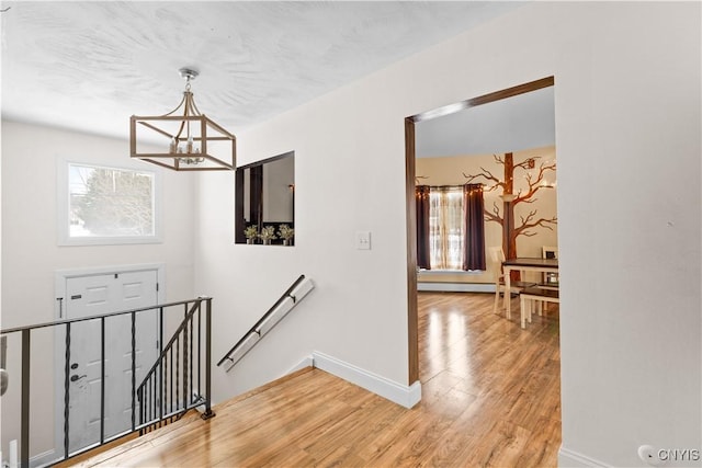 stairs featuring wood-type flooring, baseboard heating, and a chandelier