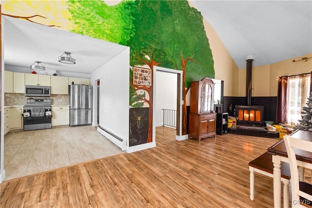 kitchen featuring a wood stove, a baseboard radiator, cream cabinetry, light hardwood / wood-style floors, and stainless steel appliances