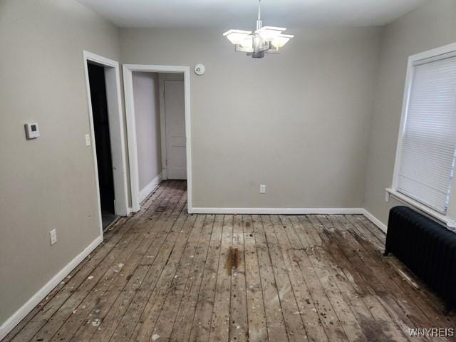 unfurnished dining area featuring a chandelier, dark hardwood / wood-style floors, and radiator