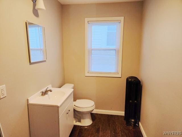 bathroom with hardwood / wood-style flooring, radiator heating unit, vanity, and toilet