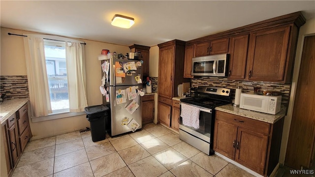 kitchen with backsplash, a wealth of natural light, light stone countertops, and stainless steel appliances