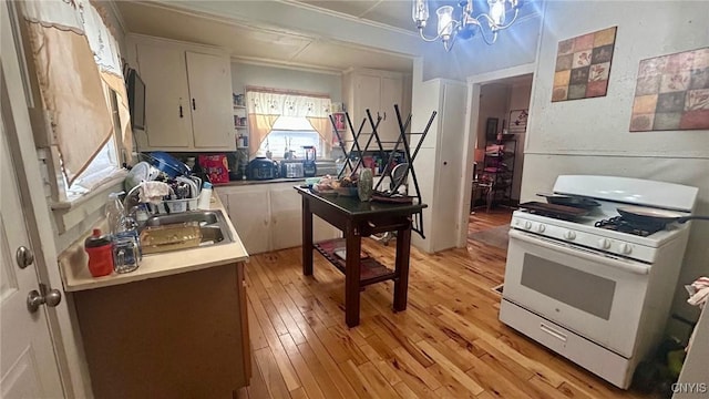 kitchen featuring light hardwood / wood-style floors, white range with gas cooktop, a notable chandelier, sink, and white cabinetry