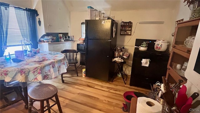 kitchen with white cabinets, black fridge, and light hardwood / wood-style floors