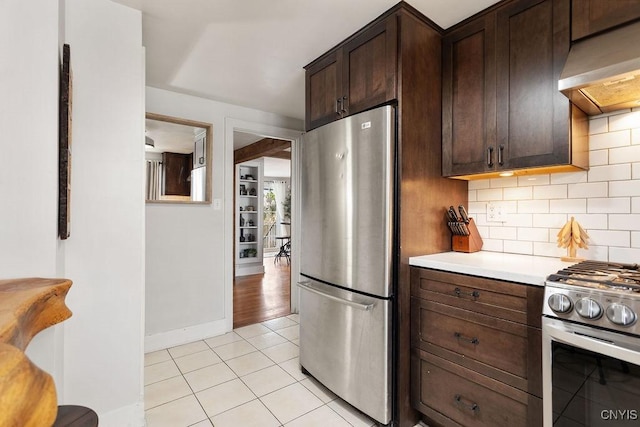 kitchen featuring premium range hood, light tile patterned floors, backsplash, appliances with stainless steel finishes, and dark brown cabinets