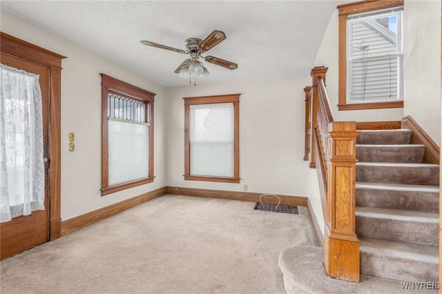 staircase with a textured ceiling, ceiling fan, and carpet flooring