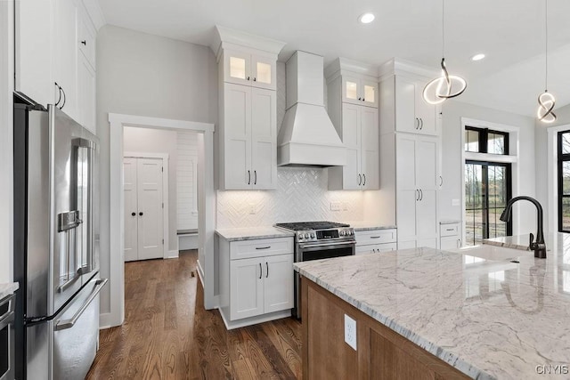 kitchen featuring custom exhaust hood, decorative light fixtures, stainless steel appliances, white cabinetry, and sink