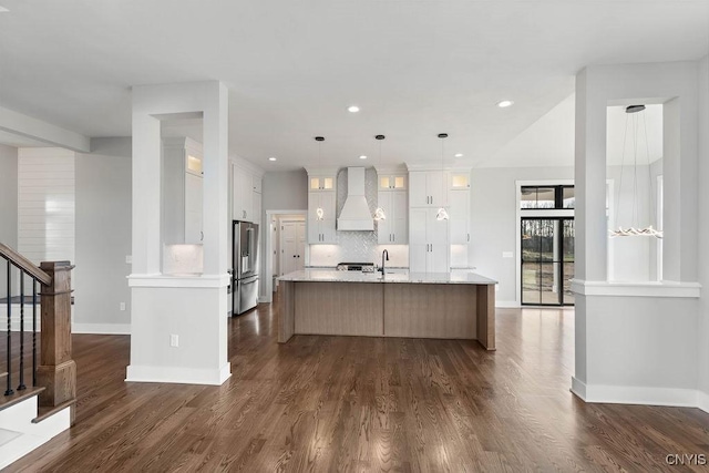 kitchen with custom exhaust hood, an island with sink, decorative backsplash, white cabinets, and high end refrigerator