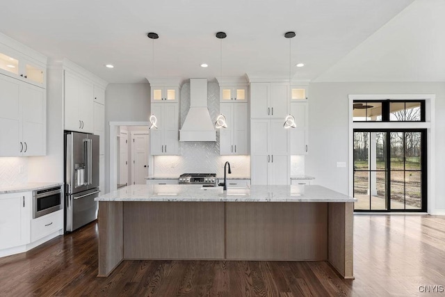 kitchen featuring custom range hood, a kitchen island with sink, white cabinetry, appliances with stainless steel finishes, and sink