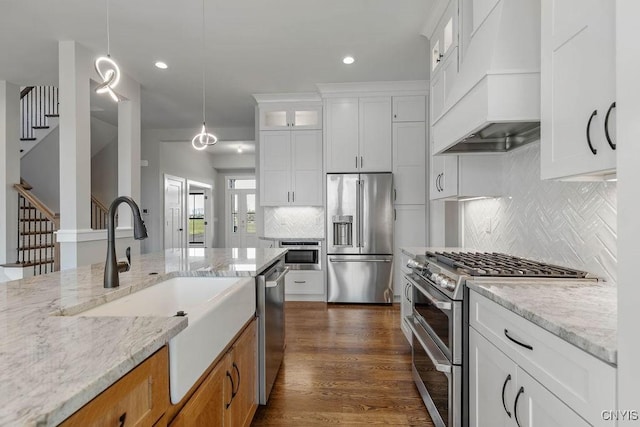 kitchen with appliances with stainless steel finishes, hanging light fixtures, premium range hood, light stone counters, and white cabinets