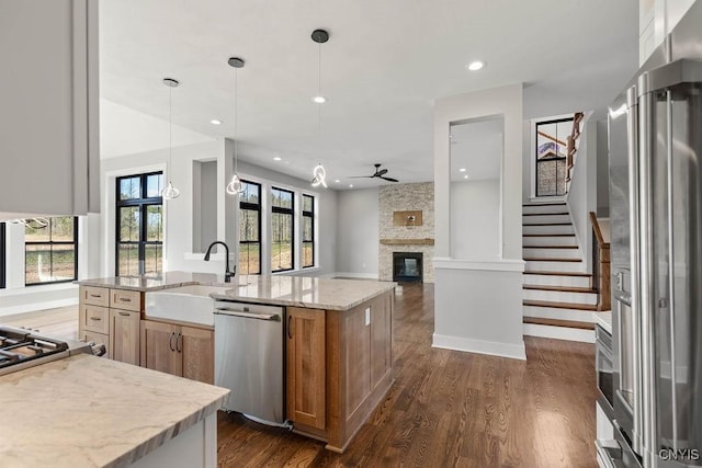 kitchen featuring pendant lighting, a stone fireplace, stainless steel appliances, a center island with sink, and sink