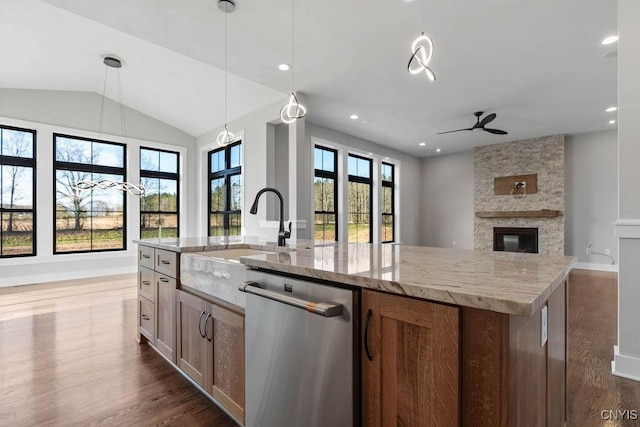 kitchen with light stone counters, stainless steel dishwasher, a center island with sink, and hanging light fixtures