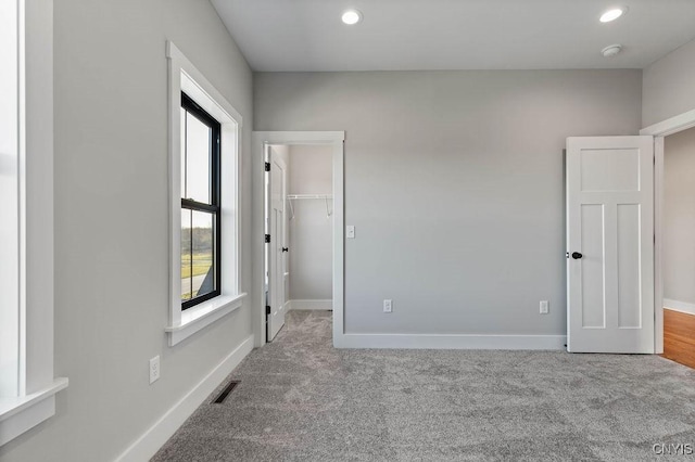 unfurnished bedroom with light colored carpet, a closet, and a spacious closet