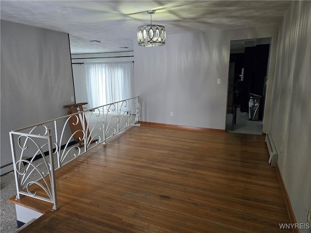 spare room with a notable chandelier, dark wood-type flooring, and a baseboard radiator