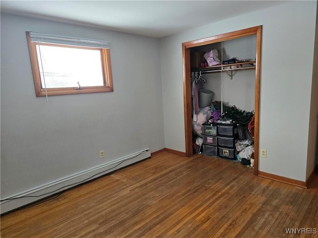 unfurnished bedroom featuring a closet, a baseboard heating unit, and hardwood / wood-style flooring