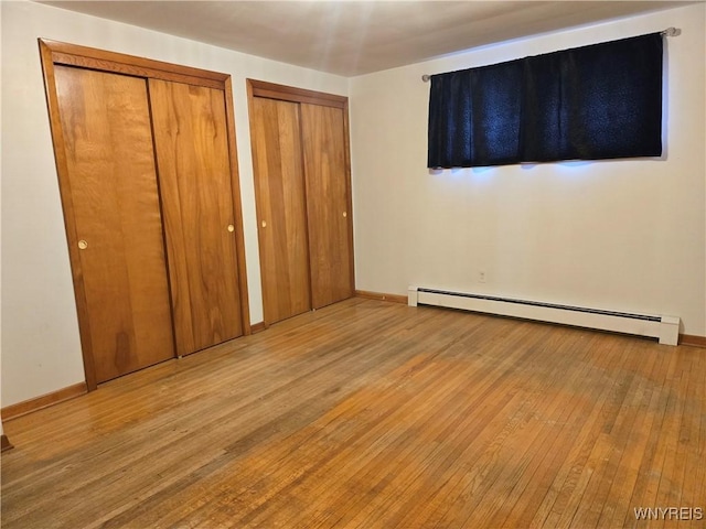 unfurnished bedroom featuring baseboard heating, hardwood / wood-style flooring, and multiple closets