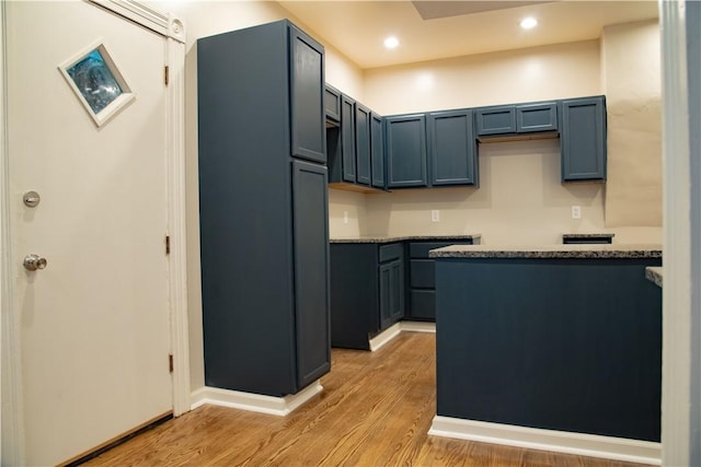 kitchen featuring paneled built in fridge, blue cabinets, light hardwood / wood-style floors, and dark stone countertops