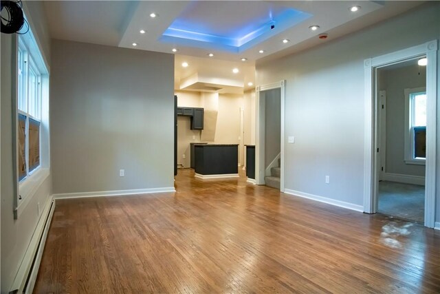 unfurnished living room with baseboard heating, a raised ceiling, and hardwood / wood-style flooring