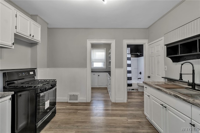 kitchen with hardwood / wood-style floors, white cabinets, black gas range oven, and sink