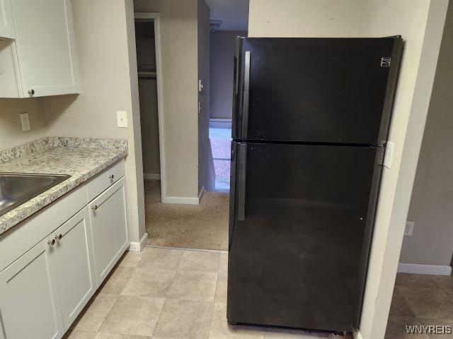 kitchen featuring black fridge, light stone countertops, sink, and white cabinetry