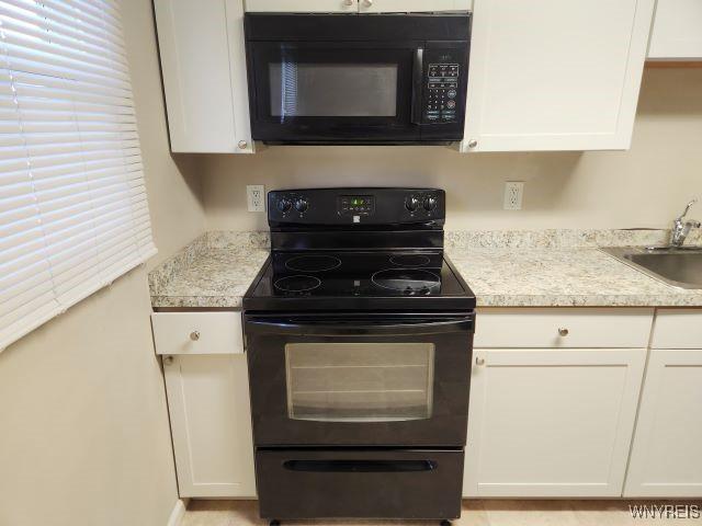 kitchen featuring sink, light stone countertops, black appliances, and white cabinetry